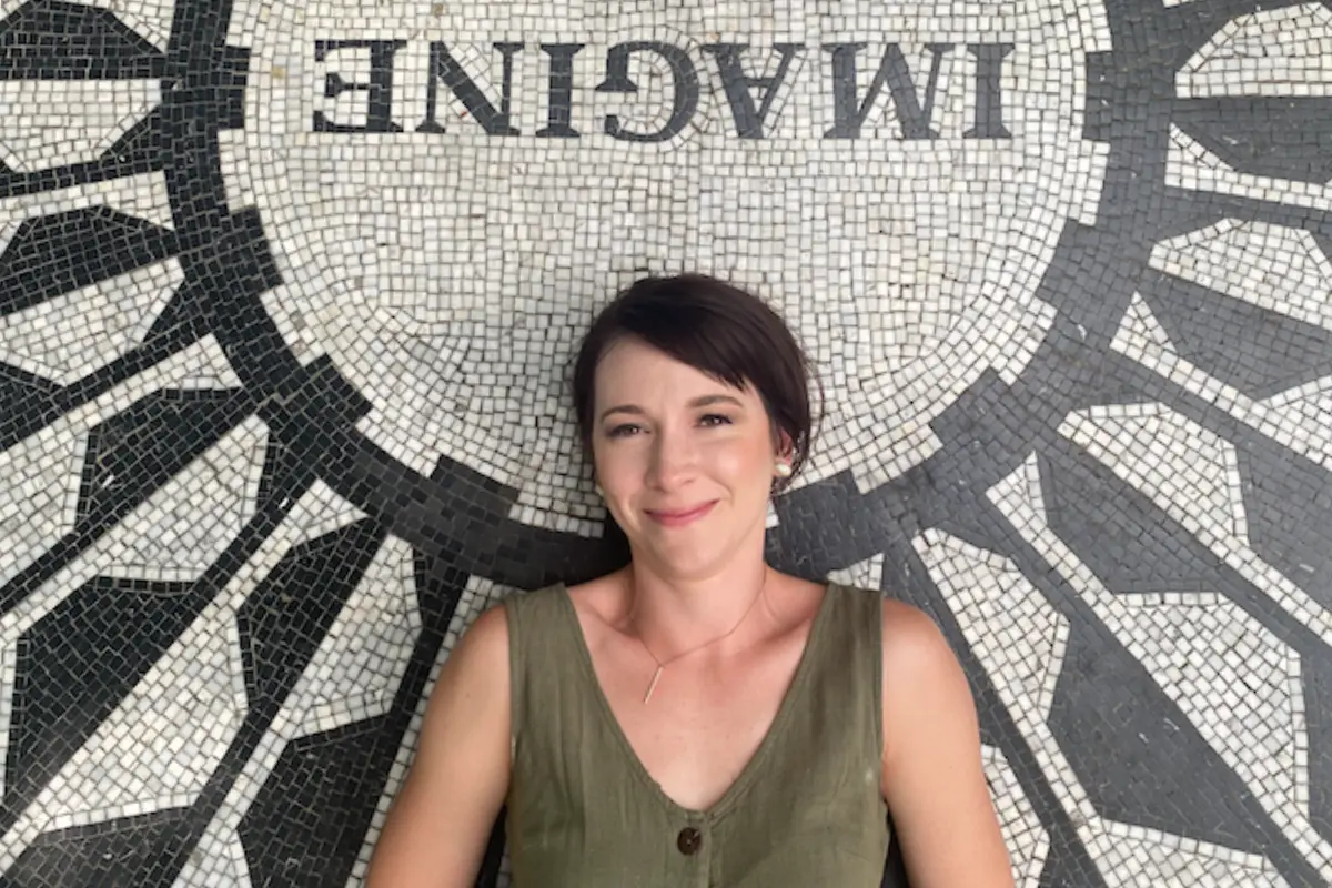 A woman with short dark hair is lying on a mosaic floor that spells out "IMAGINE." She is smiling gently and wearing a sleeveless olive green top. The image exudes a calm and reflective atmosphere, suitable for someone making money after taking a "side hustle course."