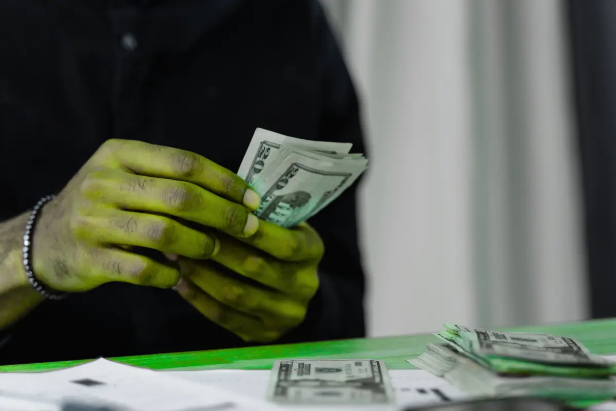 Person counting a stack of US dollar bills at a desk, symbolizing intentional money habits and personal finance management.