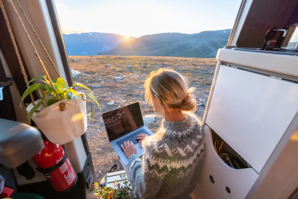 Woman working remotely on a laptop in a camper van at sunrise, representing freedom and flexibility from pursuing ideas for a side hustle.