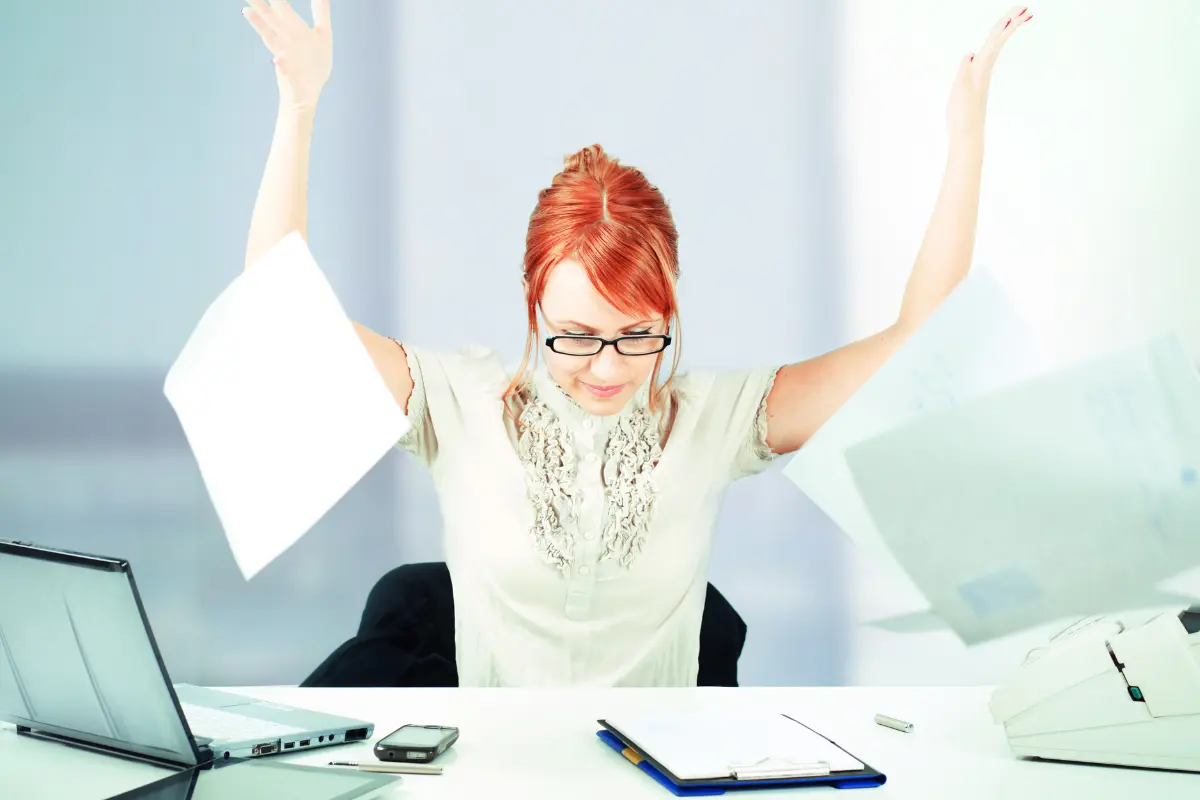 Woman throwing papers in the air joyfully at her desk symbolizing the freedom of retiring early
