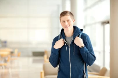 Young man in a hoodie with a backpack, smiling confidently indoors—representing simple and lazy side hustle ideas for students or beginners.