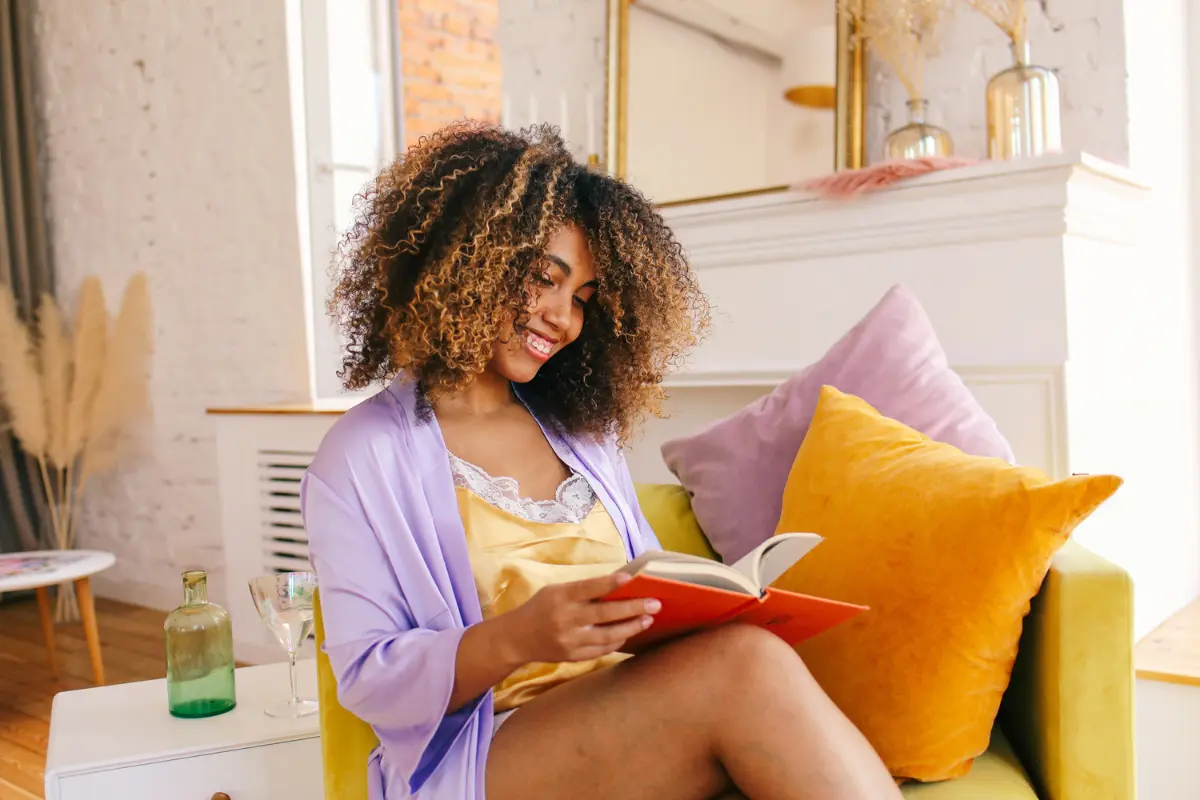 Woman smiling while reading a book at home, learning how to create passive income in a cozy, relaxed setting