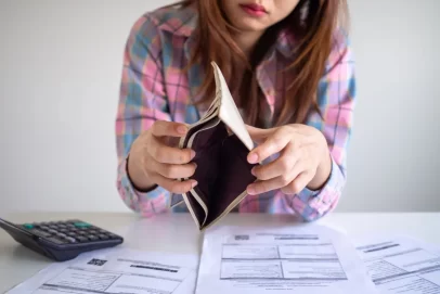 Woman holding an empty wallet while looking at unpaid bills, symbolizing financial struggles and the need to learn how to create passive income with no money.