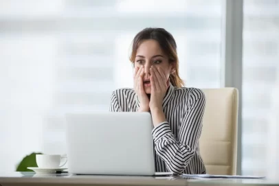 A stressed young woman in front of a laptop, holding her face in frustration—illustrating the challenges and mistakes behind why most side hustles fail.