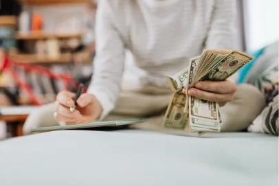 Person counting cash and taking financial notes, representing practical budgeting and smart money habits — concept for “10 Proven Money Habits That Will Make You Richer This Year.”