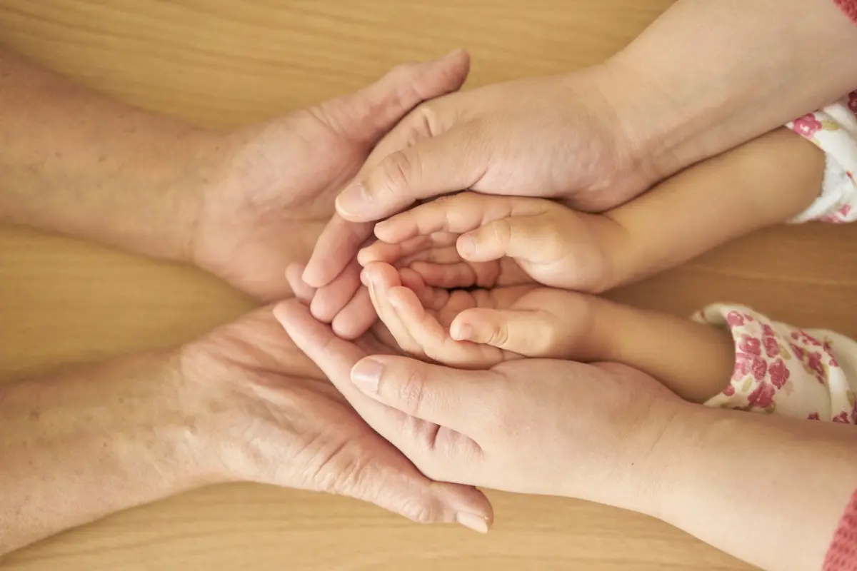 Close-up of three generations’ hands gently stacked together, symbolizing family legacy and long-term financial security — perfect for illustrating 7 Everyday Money Rituals That Quietly Build Generational Wealth Now.