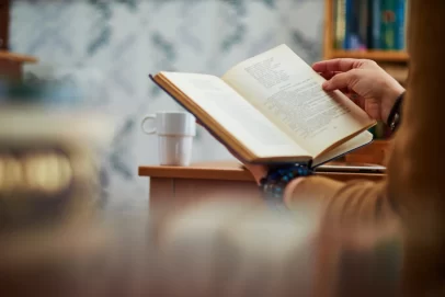 Person reading a book with a coffee mug on the table nearby, symbolizing reflection, learning, and life philosophy — perfect for illustrating Die With Zero Summary.