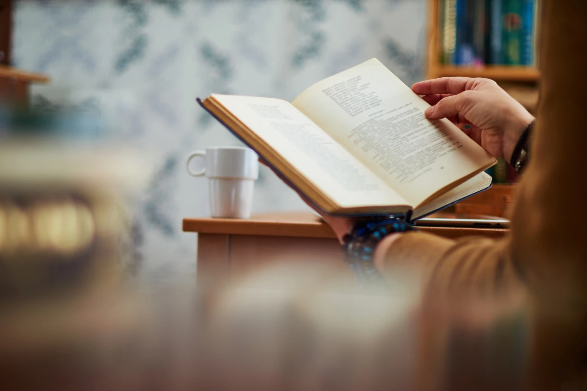 Person reading a book with a coffee mug on the table nearby, symbolizing reflection, learning, and life philosophy — perfect for illustrating Die With Zero Summary.
