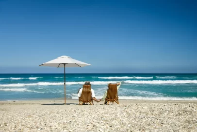 Couple relaxing on beach chairs under an umbrella, holding hands while enjoying the ocean view — symbolizing financial freedom and early retirement. Perfect for illustrating This Simple Strategy Lets You Retire 15 Years Early.