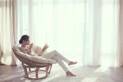 Woman relaxing in a cozy chair by a bright window, sipping coffee and reading a book — symbolizing calm clarity and focus in mastering the Ultimate Money Blueprint.