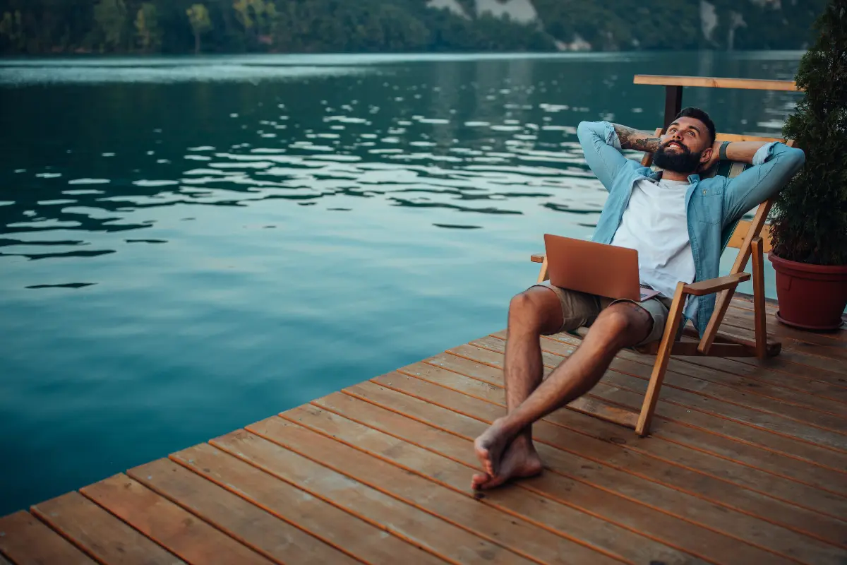 Man relaxing on a lakeside deck with a laptop, symbolizing freedom and flexibility — concept image for easy businesses that allow you to work from anywhere.
