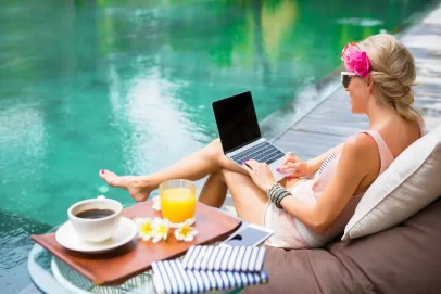 Woman working on a laptop by a pool with coffee and juice, representing financial freedom and lifestyle flexibility.