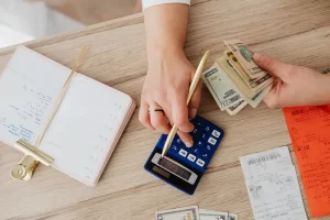 Person using a calculator and counting cash at a desk, representing strategies to build passive income through budgeting and financial planning.