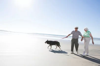 Active senior couple walking their dog on the beach, representing financial freedom through smart side hustle ideas.