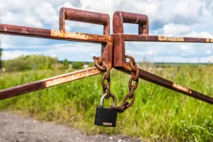 Rusted metal gate chained and locked in a rural field, symbolizing barriers to passive income and financial growth.