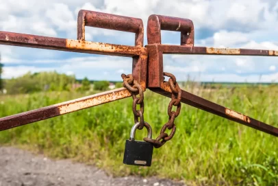 Rusted metal gate chained and locked in a rural field, symbolizing barriers to passive income and financial growth.