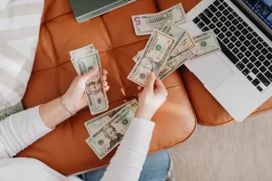Hands counting cash beside a laptop, illustrating how to create passive income from online work and digital income streams.