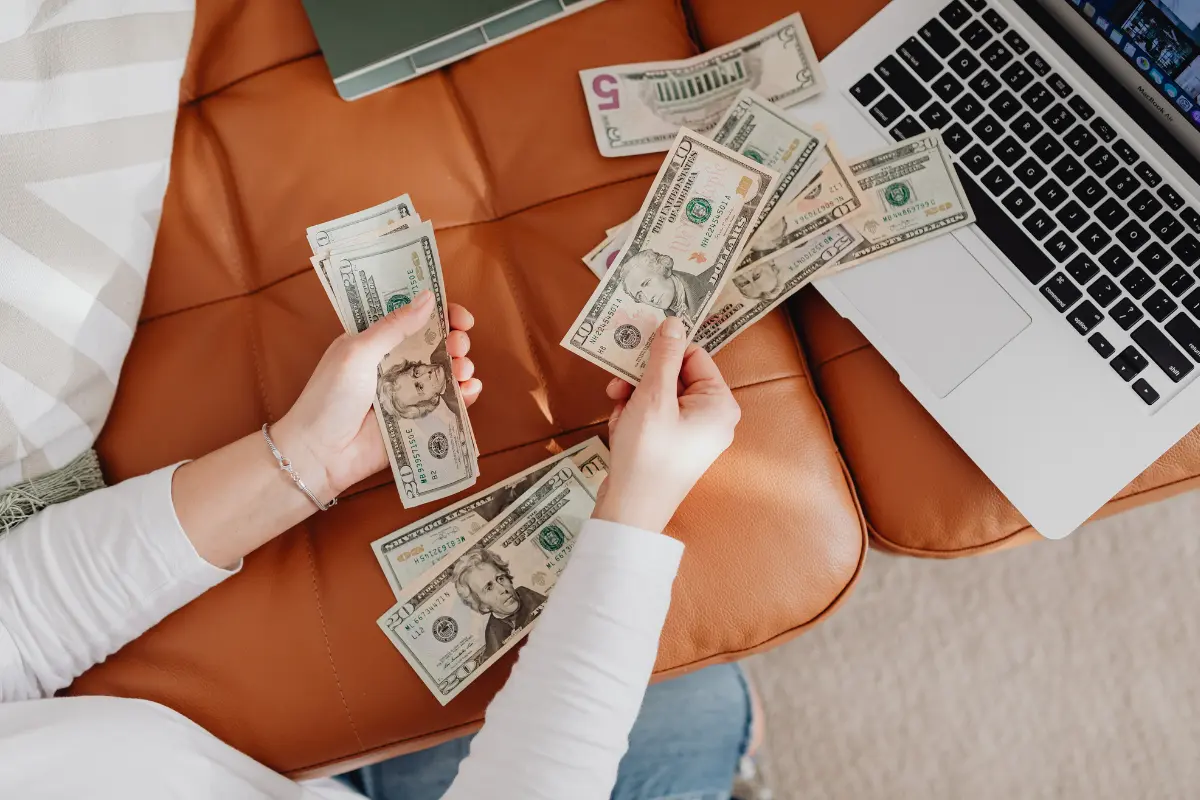 Hands counting cash beside a laptop, illustrating how to create passive income from online work and digital income streams.