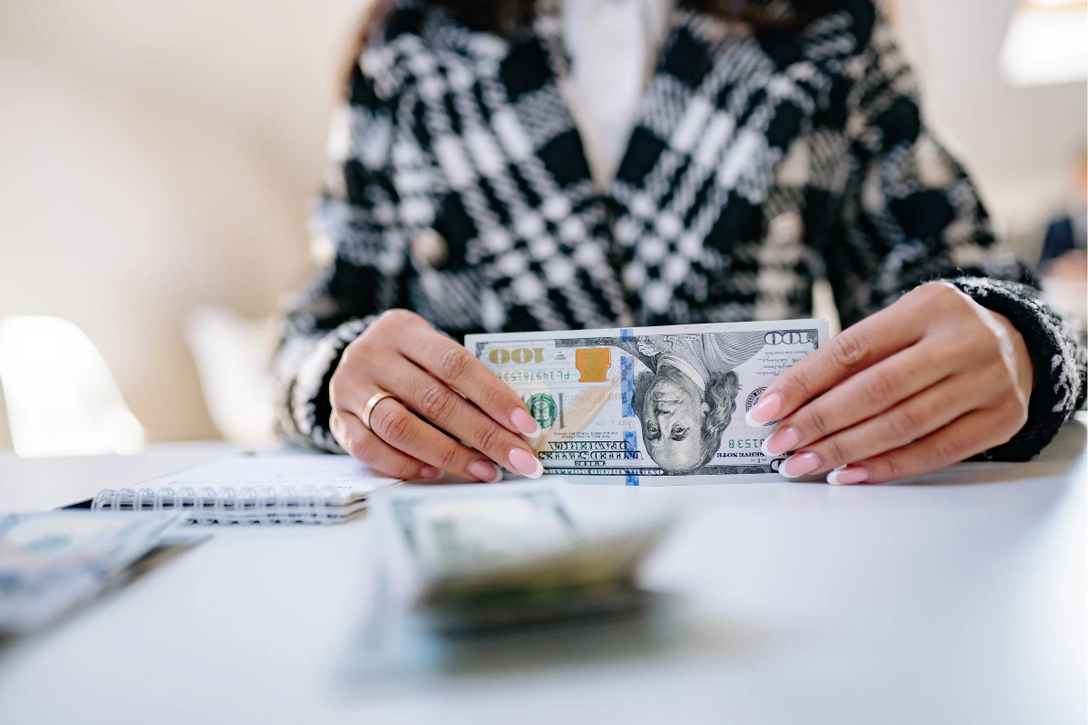 Woman holding a one hundred dollar bill at a desk, representing intentional wealth building moves and smart money decisions.