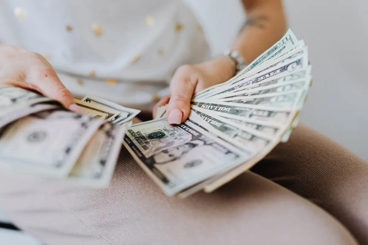 Person counting a stack of U.S. cash, illustrating how to build wealth through saving money, investing consistently, managing finances wisely, and creating long-term financial security.