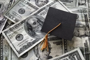 Graduation cap resting on U.S. dollar bills representing how to pay for college through savings, scholarships, investing, and financial planning