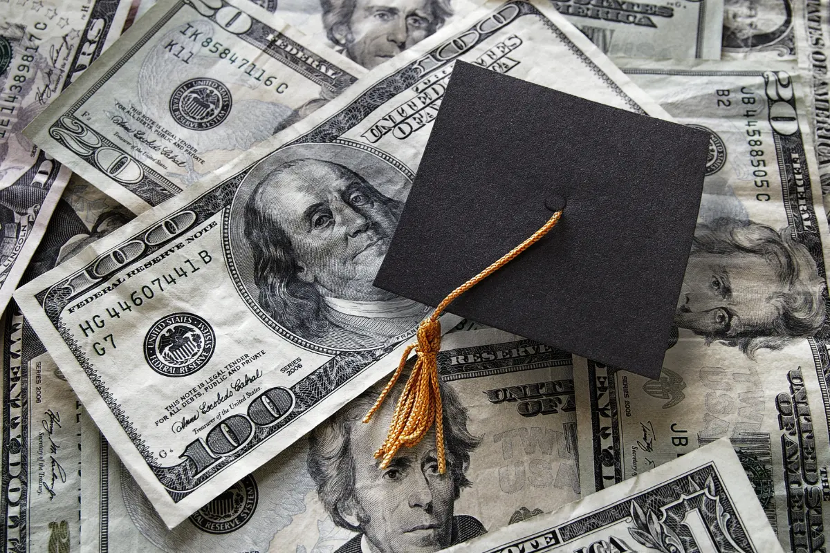 Graduation cap resting on U.S. dollar bills representing how to pay for college through savings, scholarships, investing, and financial planning